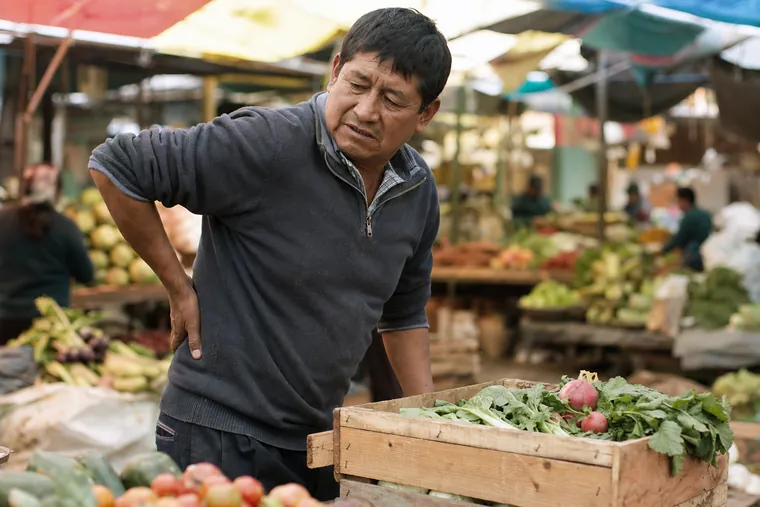 Trabajador de mercado en Perú se lleva la mano a la espalda baja tras cargar una caja